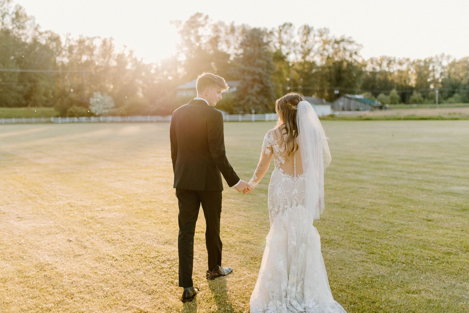Wedding couple walking hand in hand across a sunlit field at golden hour.