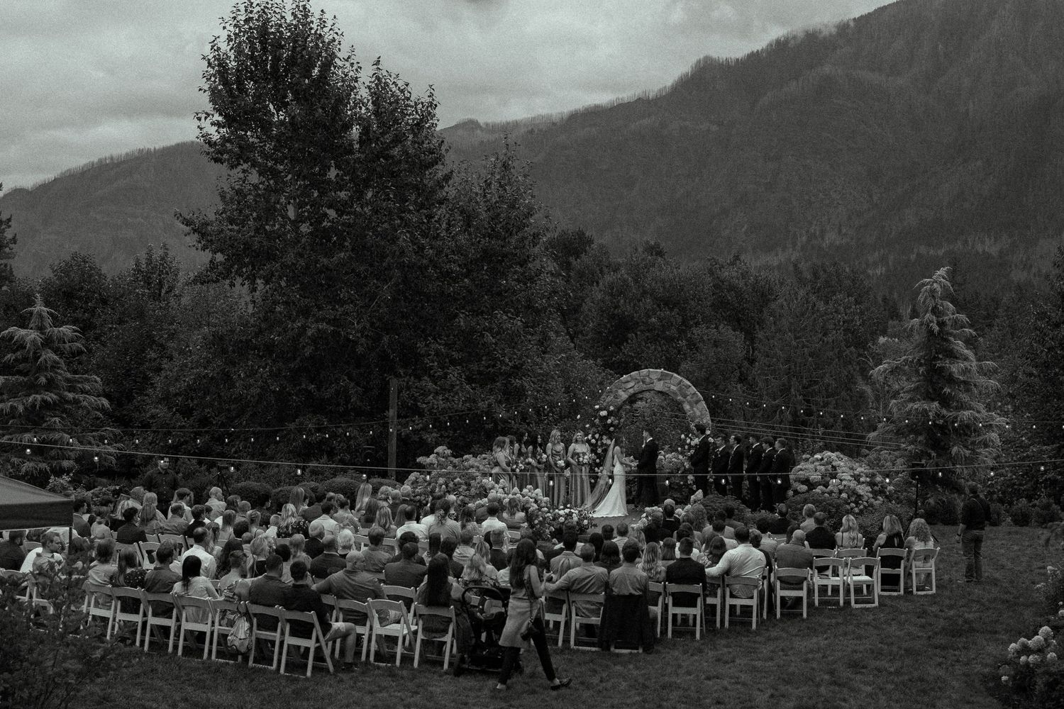 Outdoor wedding ceremony setup with rows of white chairs against a mountain backdrop.