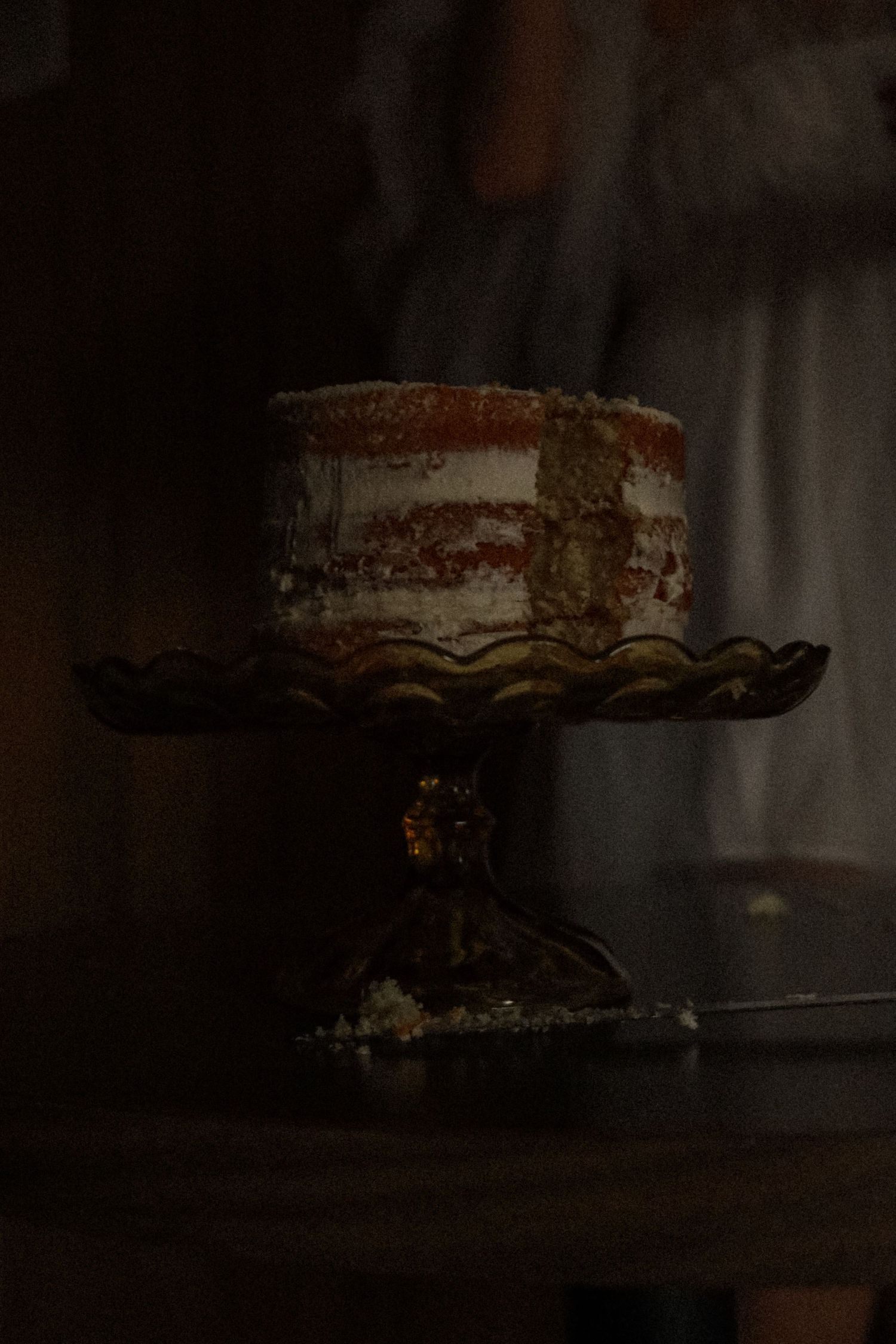 A rustic naked cake with textured frosting sits elegantly in moody lighting.