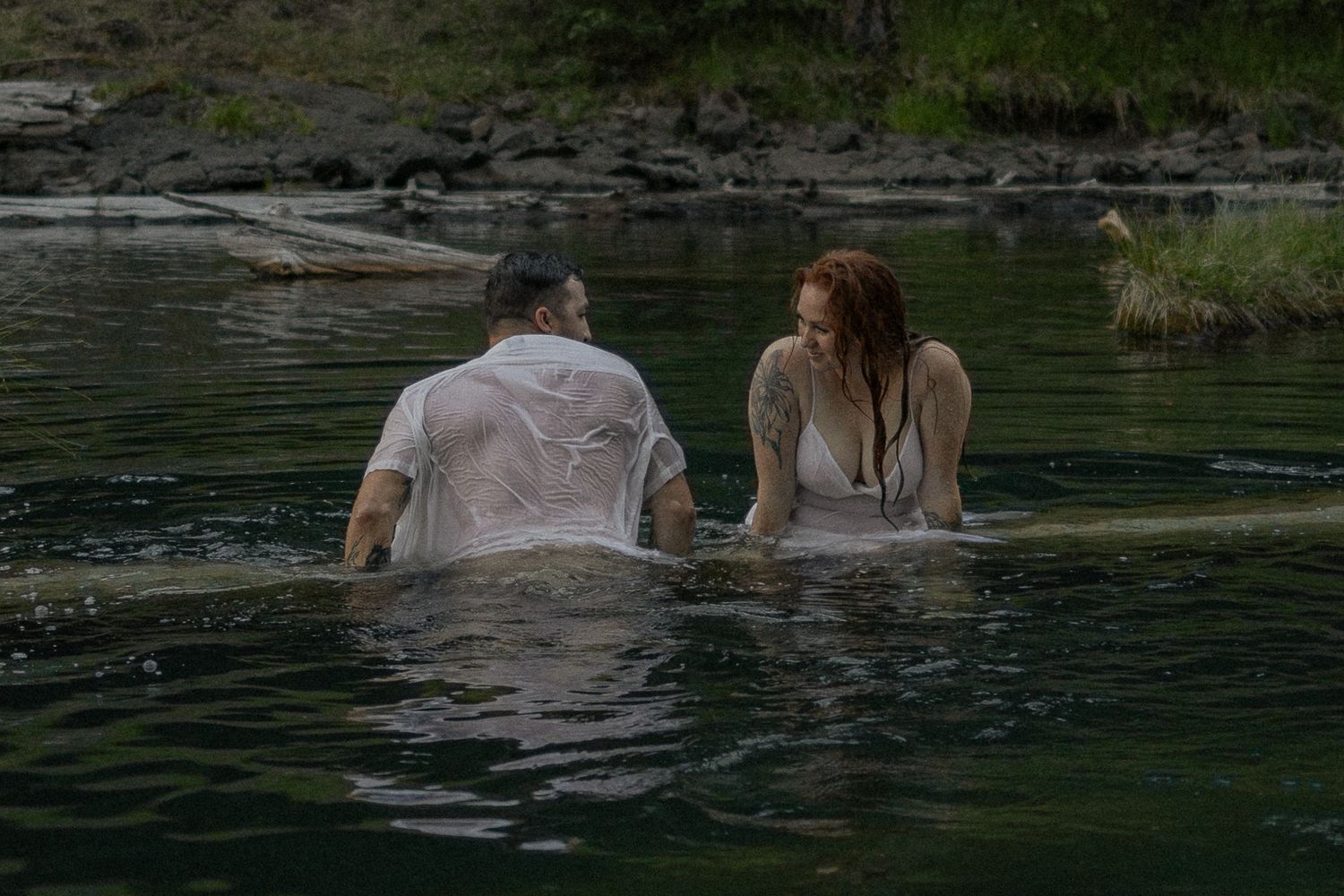 Couple enjoying a romantic swim in a serene lake surrounded by nature.