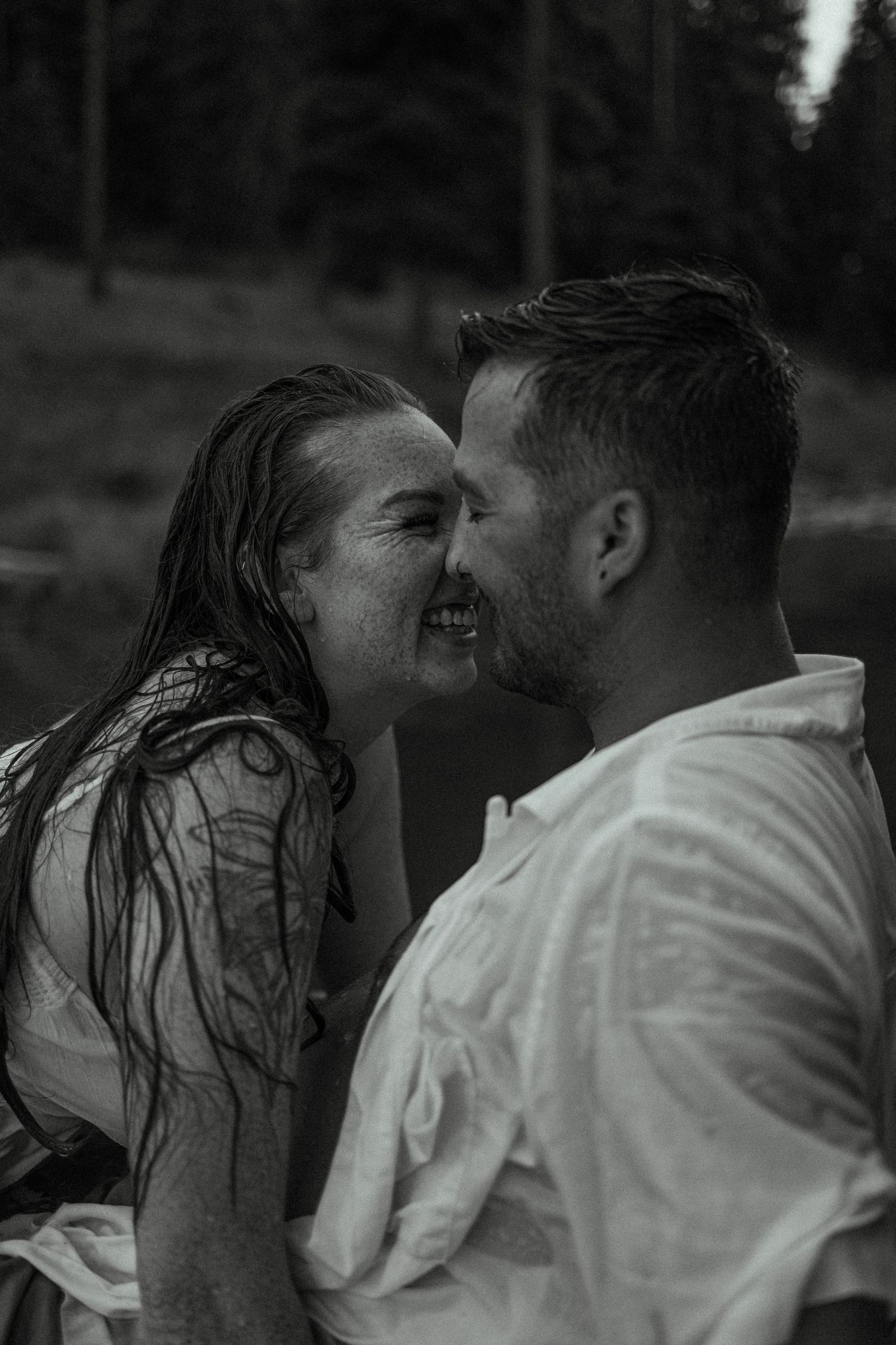 An intimate black and white portrait shows a couple sharing a joyful moment by the water.