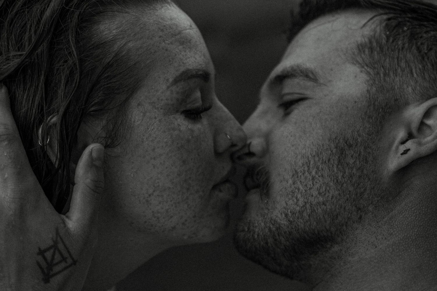 A close-up black and white photo captures an intimate kiss between a couple.