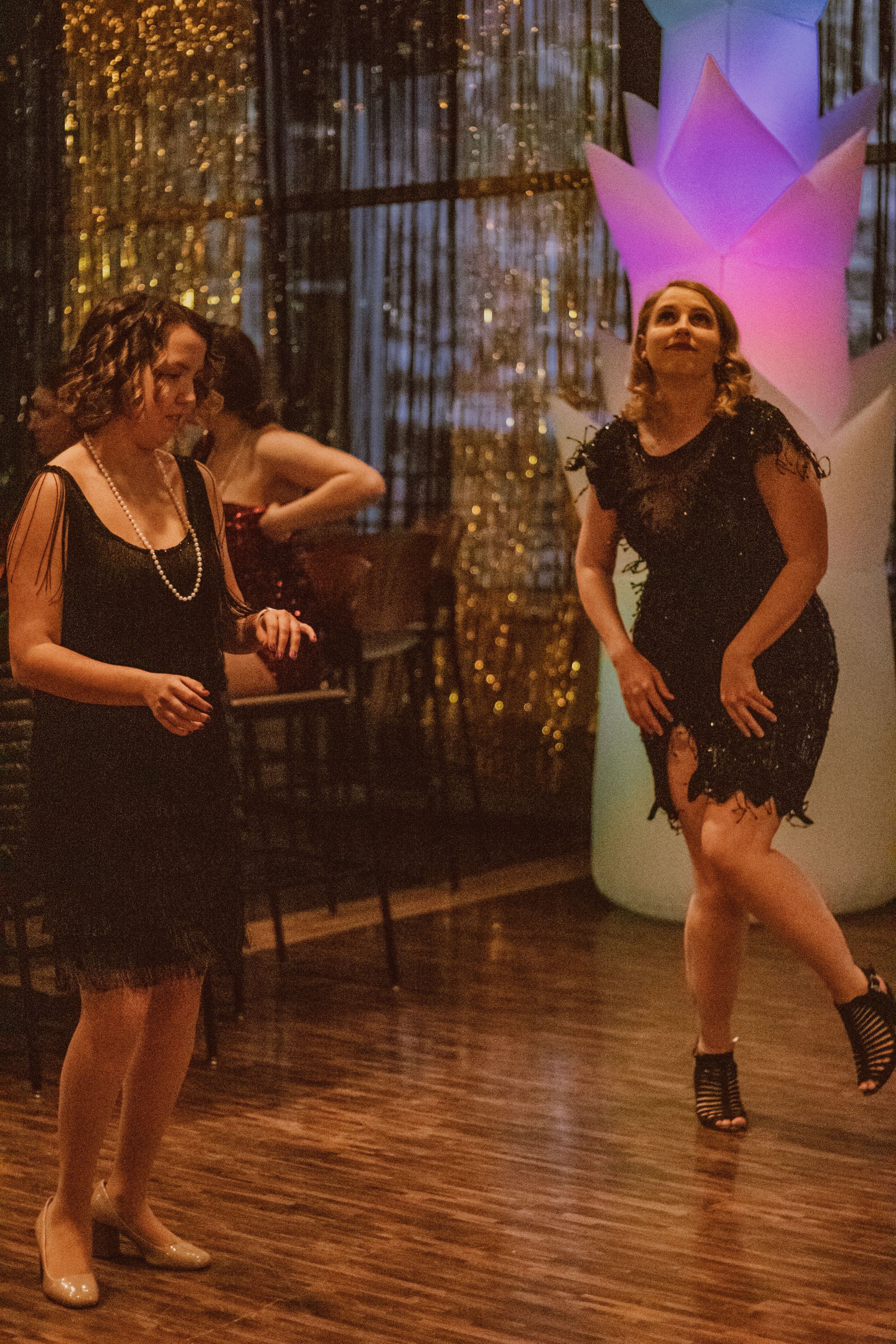 People dancing on wooden floor under colorful lights and gold decorations.