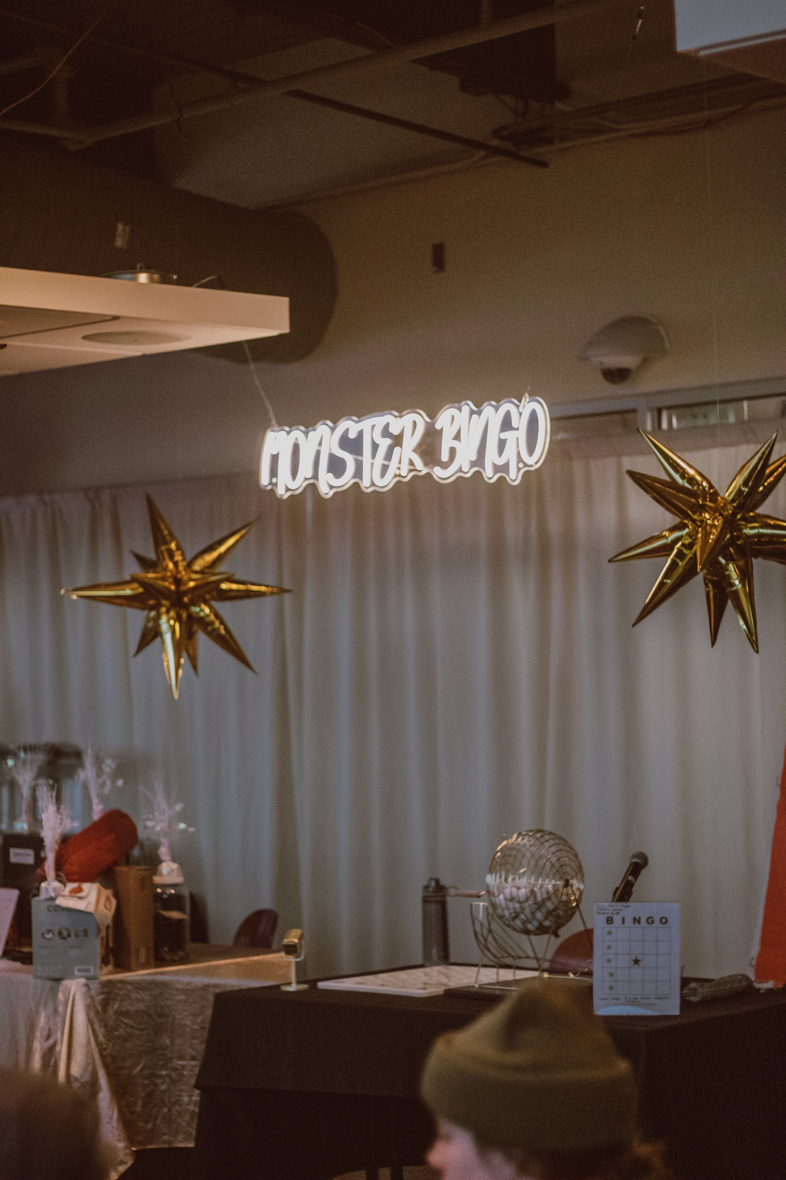 Neon sign and gold star decorations illuminate a dimly lit event space.