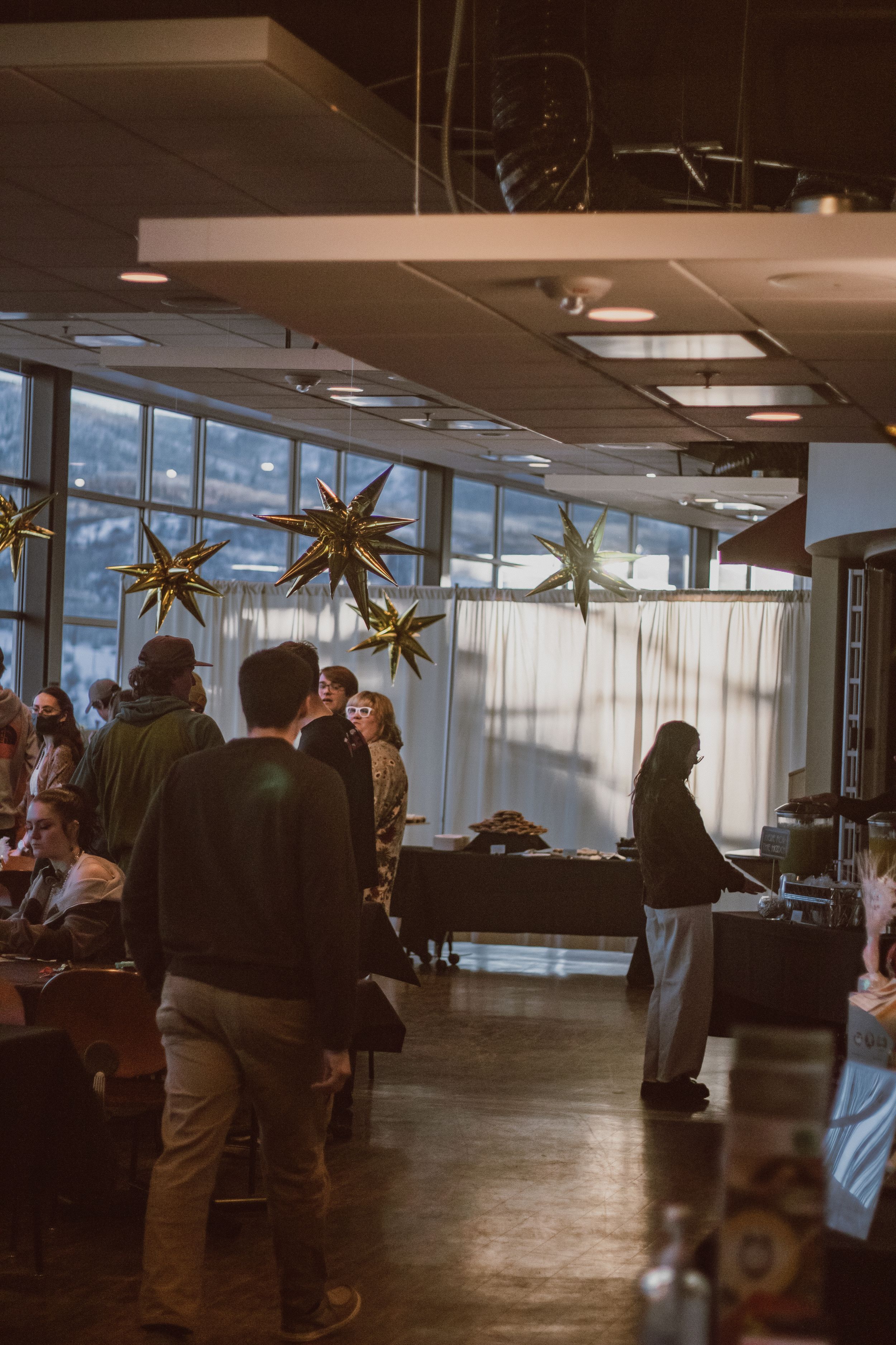 People gathering in a spacious room decorated with hanging gold star ornaments.