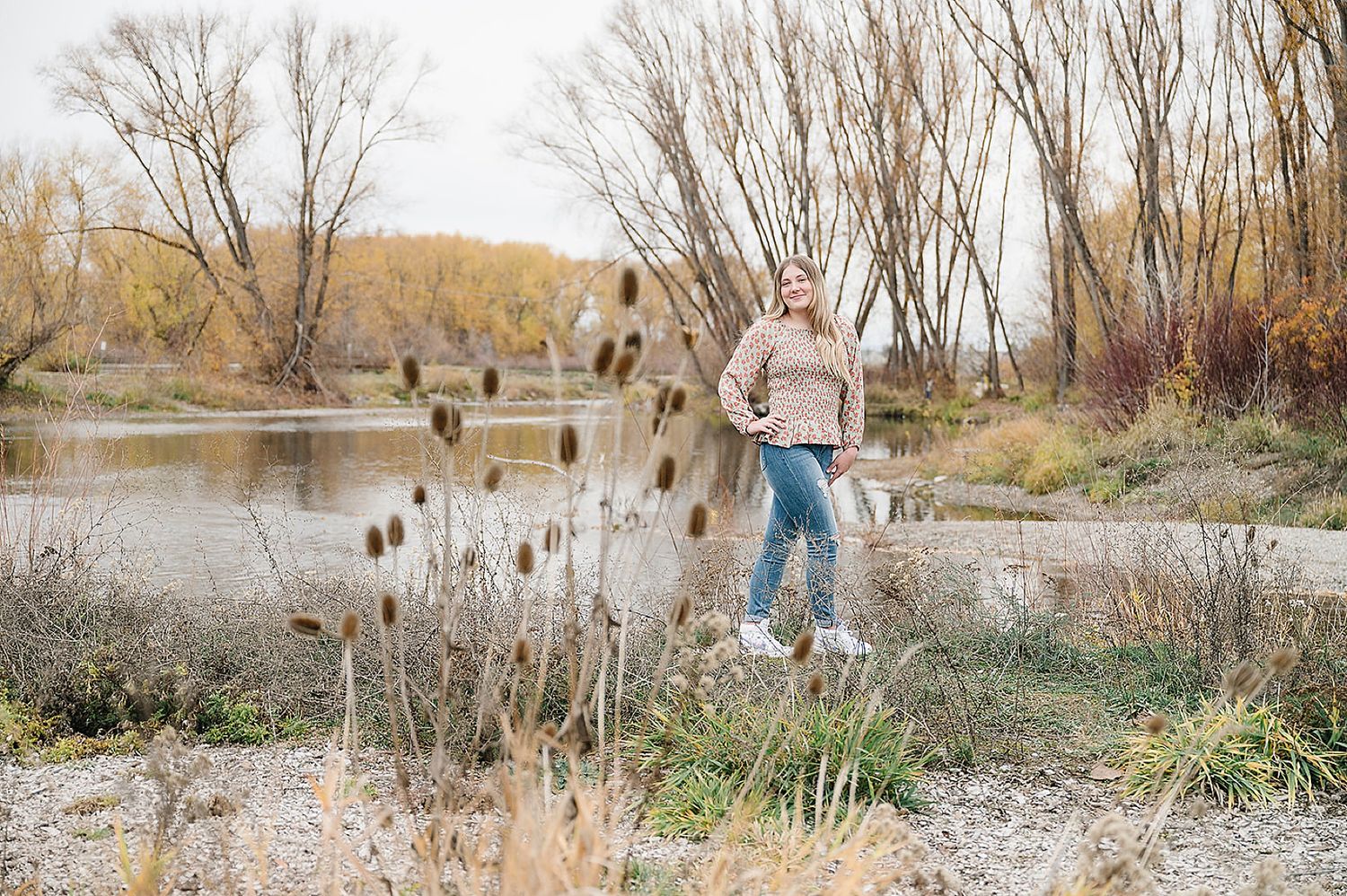 A casual outdoor portrait session near a river with cattails and bare trees in the background.