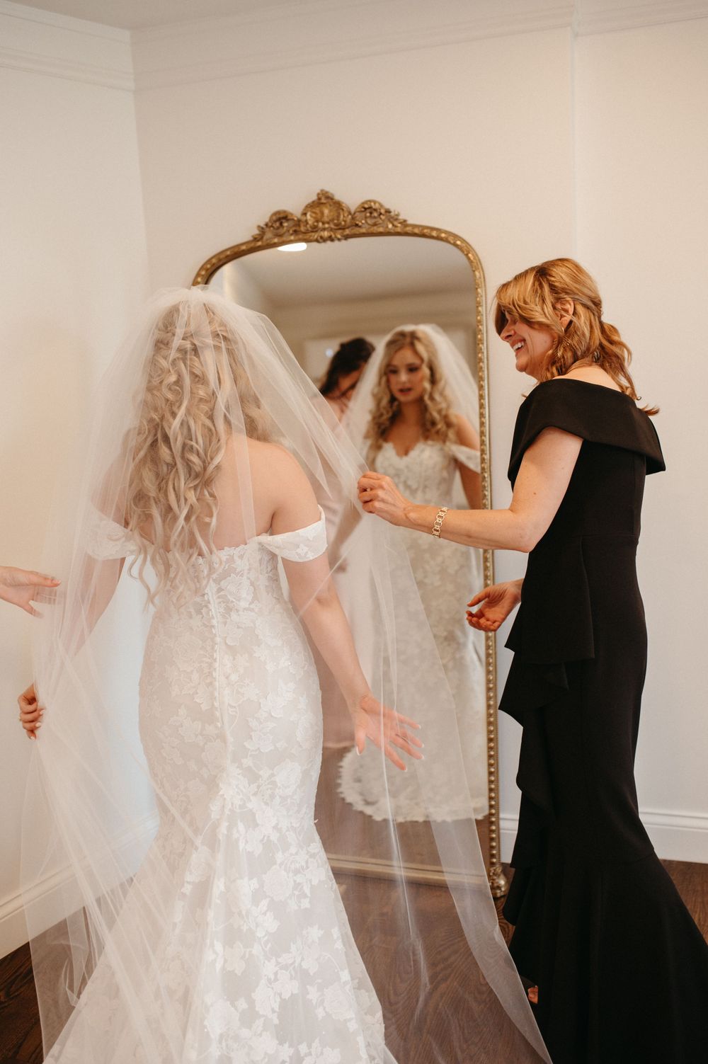 Wedding dress preparation moment reflected in an ornate gold mirror.