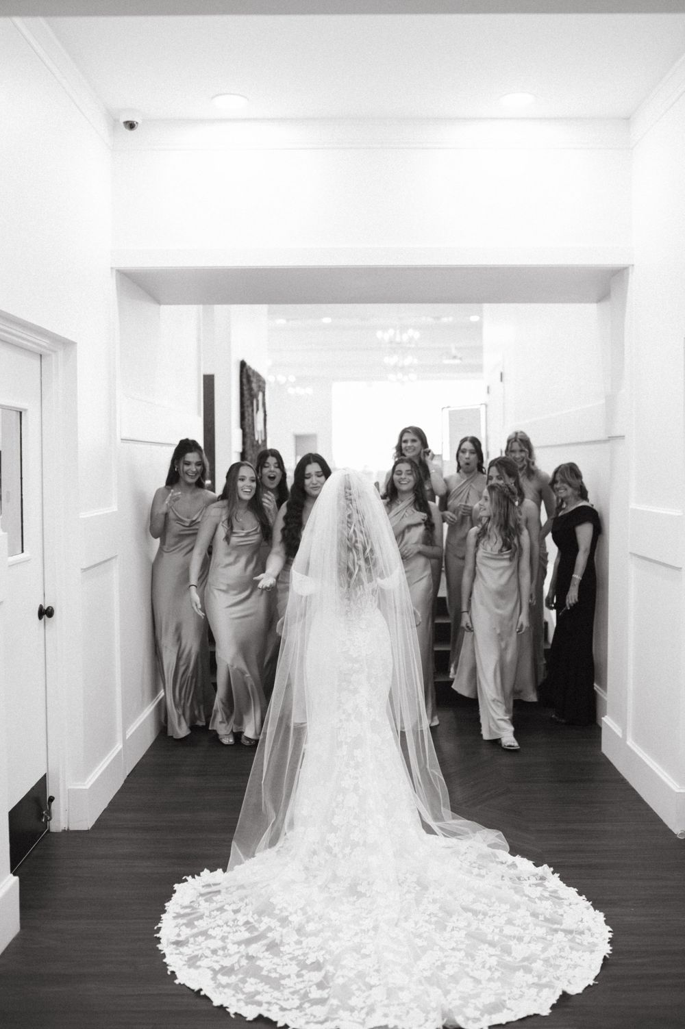Black and white wedding photo showing long veil and bridesmaids in elegant dresses.