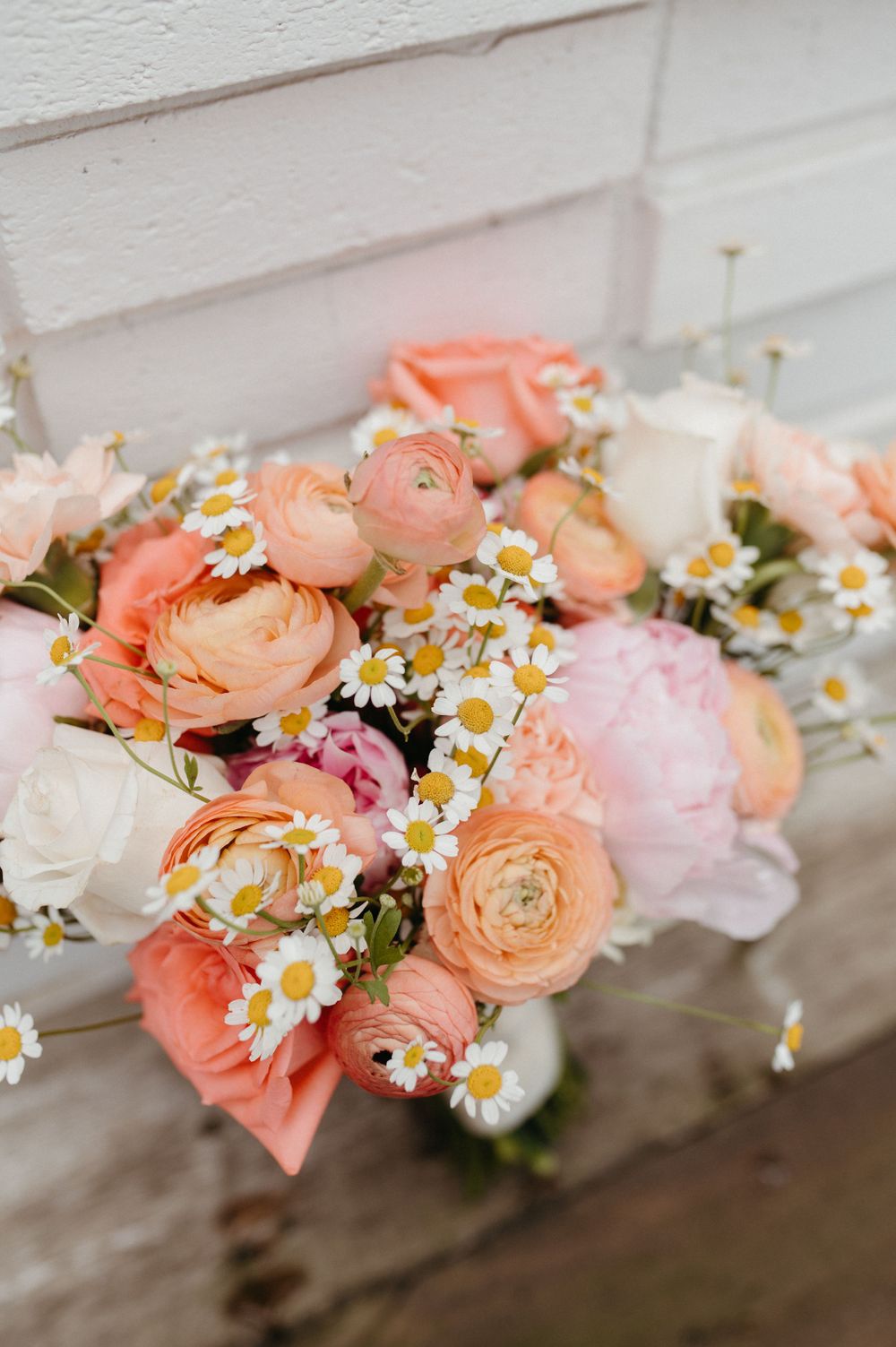 Romantic bouquet of peach ranunculus flowers and white daisies arranged in soft natural light.