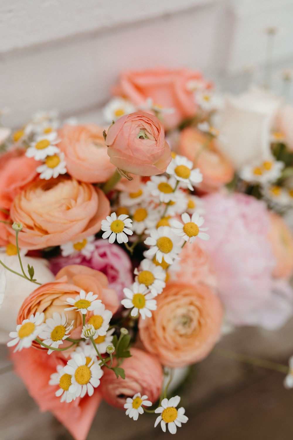 Close-up of coral ranunculus and daisy flower arrangement with delicate petals and yellow centers.