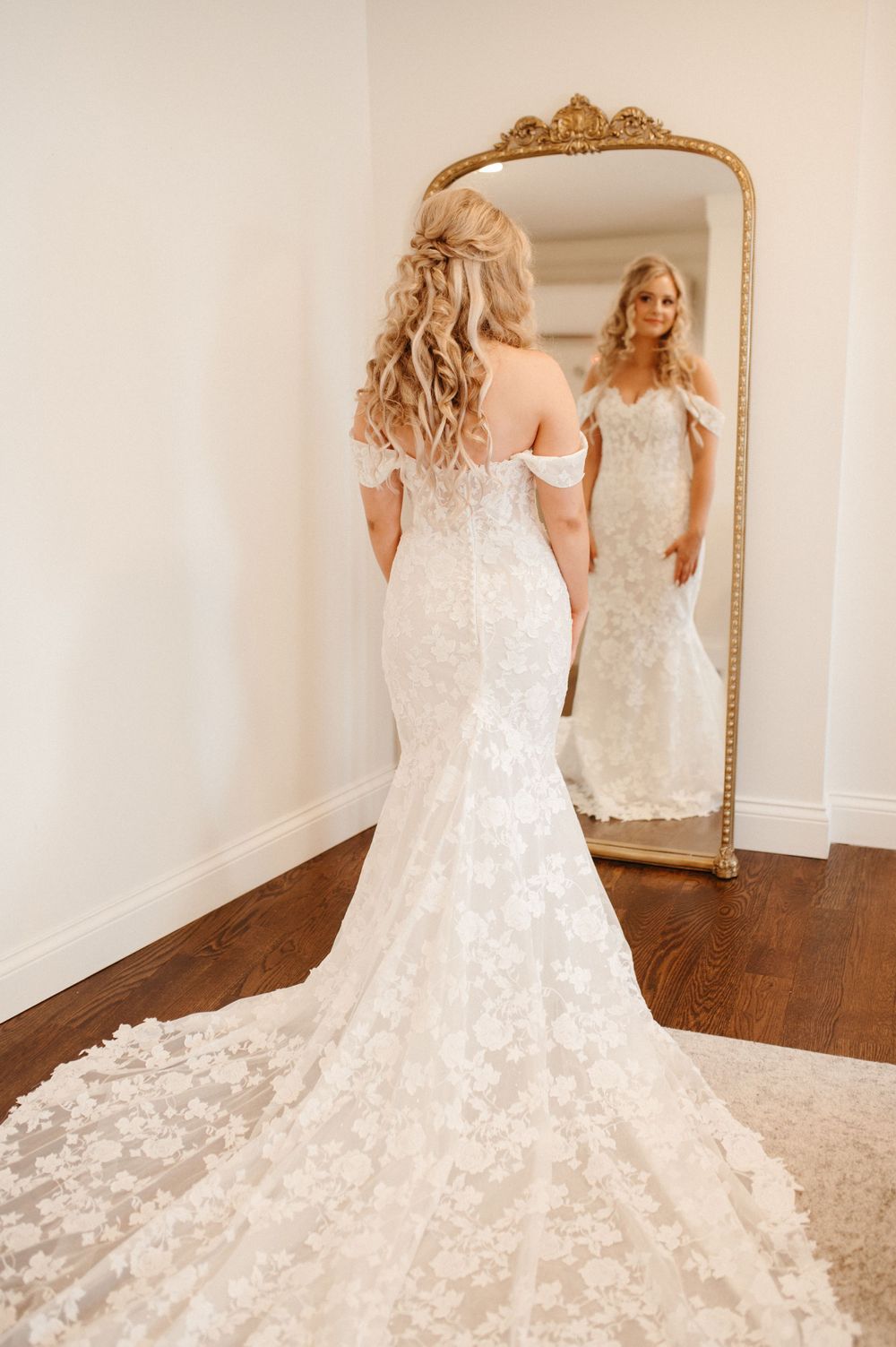 Detailed back view of lace wedding gown with long train reflected in ornate gold mirror.