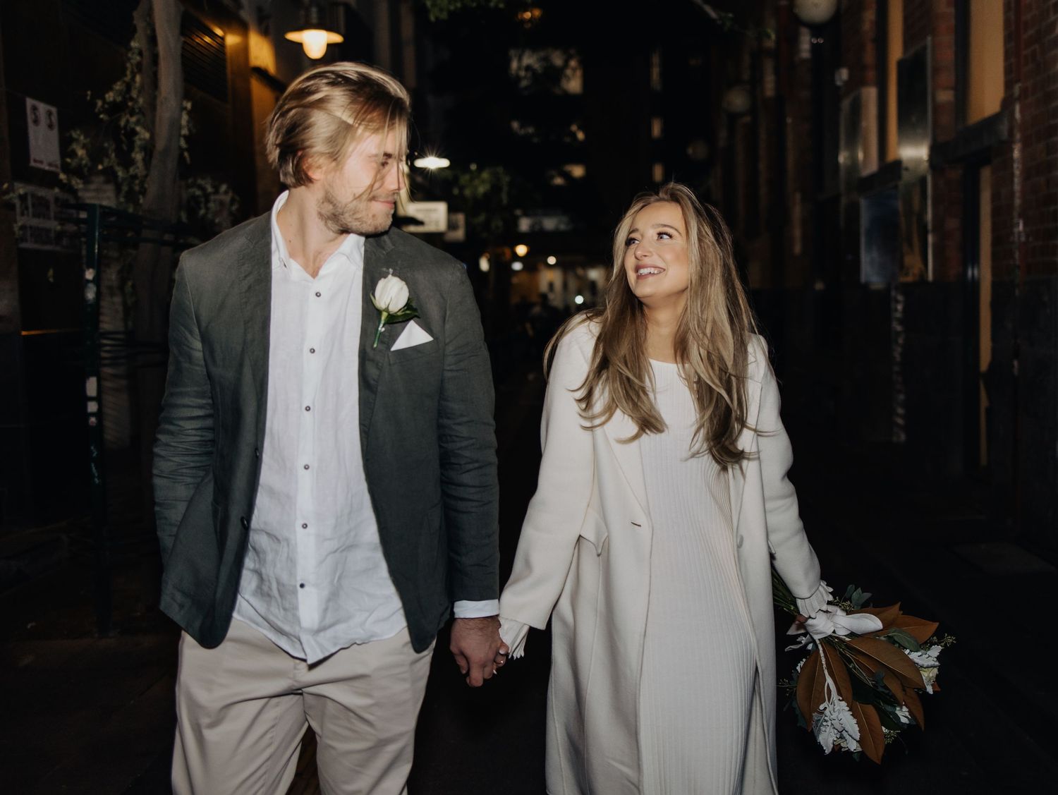 A couple in formal attire shares intimate moments against an urban backdrop at night.