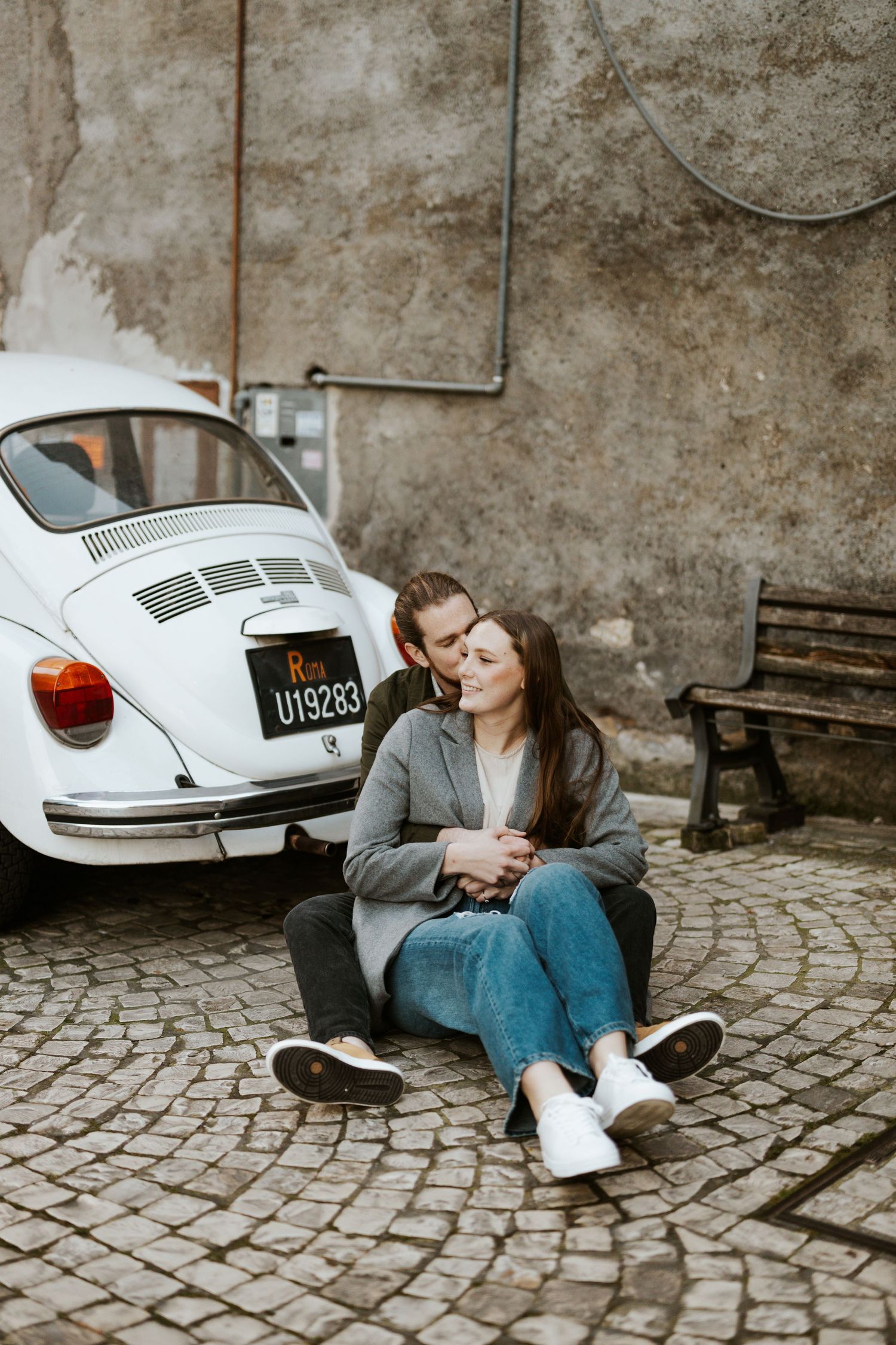 a couple sitting on the ground with a vintage car behind them near Rome, Italy during their vacation photoshoot