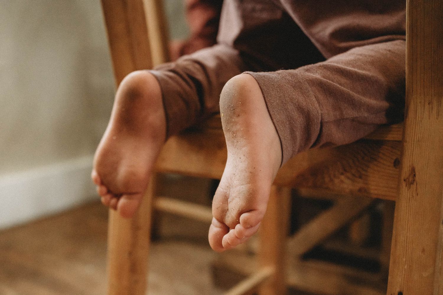 Bare feet resting on wooden chair rungs during indoor activity.