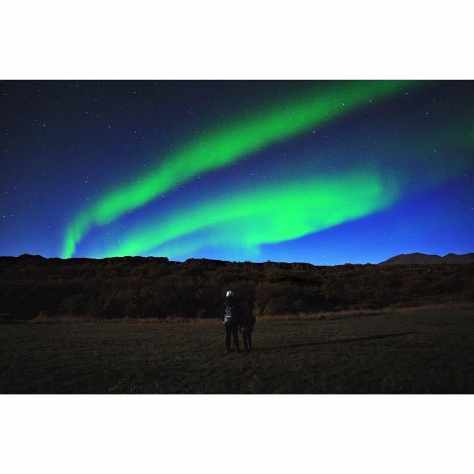A mother and daughter look at the the northern lights or Aurora borealis in a field with mountain Mosfellsdalur, Iceland