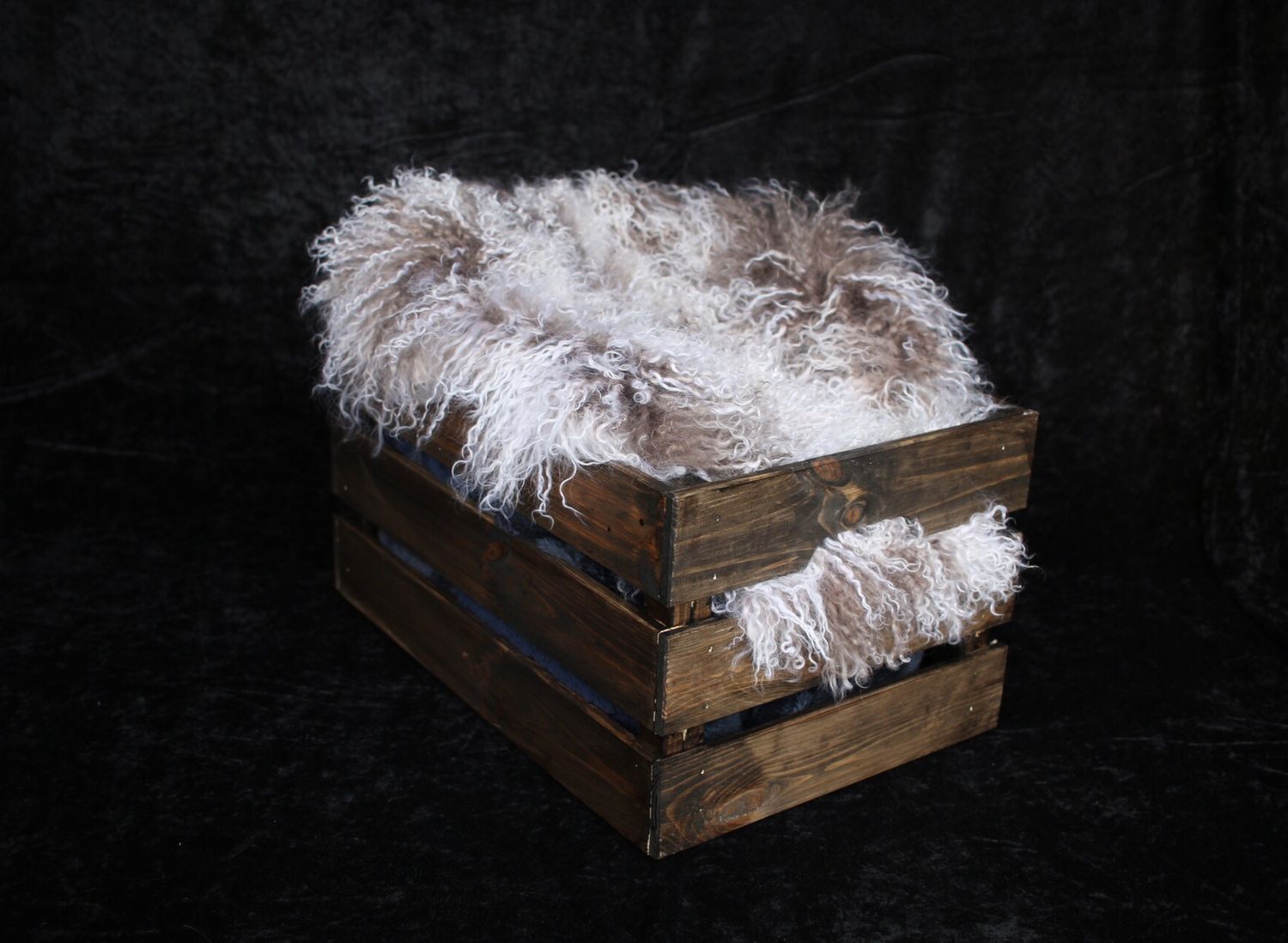 Rustic wooden crate filled with white fluffy fur material against dark background.
