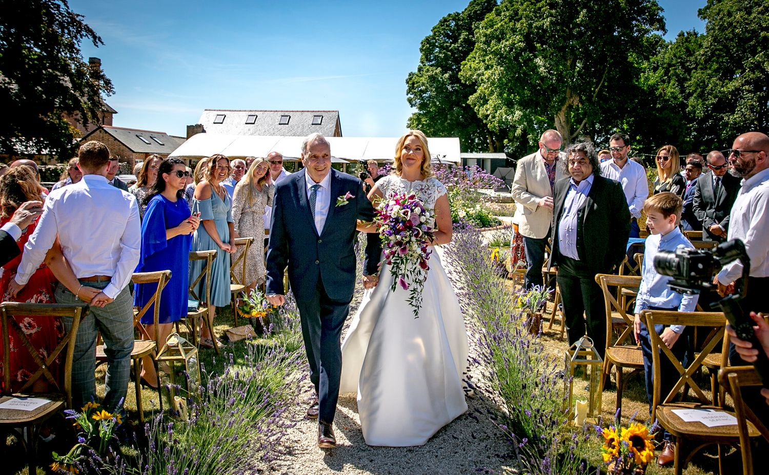 Wedding ceremony in a garden with chairs lined up along a floral-lined aisle.