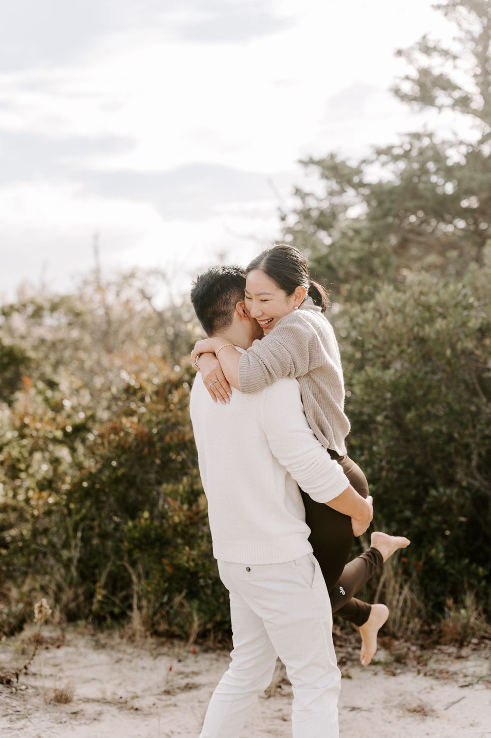 Couple in white and beige sharing playful moment on sandy path.