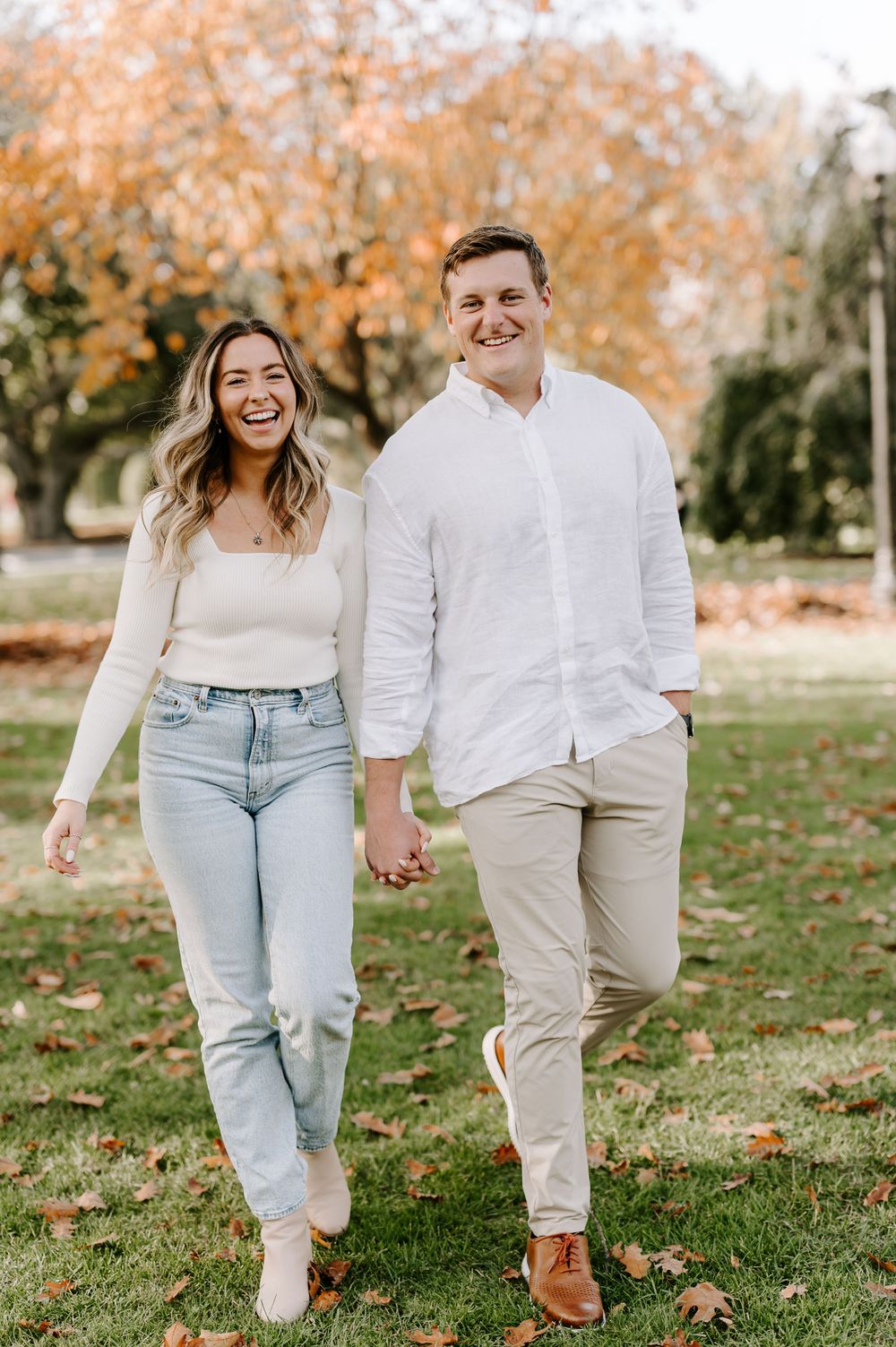 Couple walking hand in hand through a park with autumn leaves.