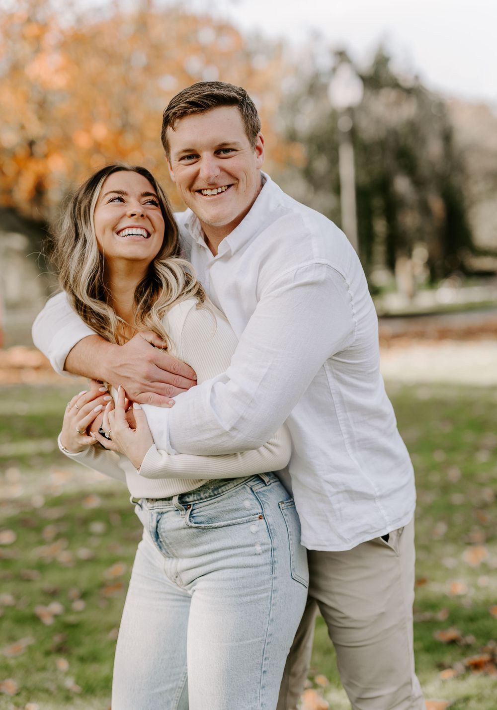 Couple laughing and embracing in a park during fall season.