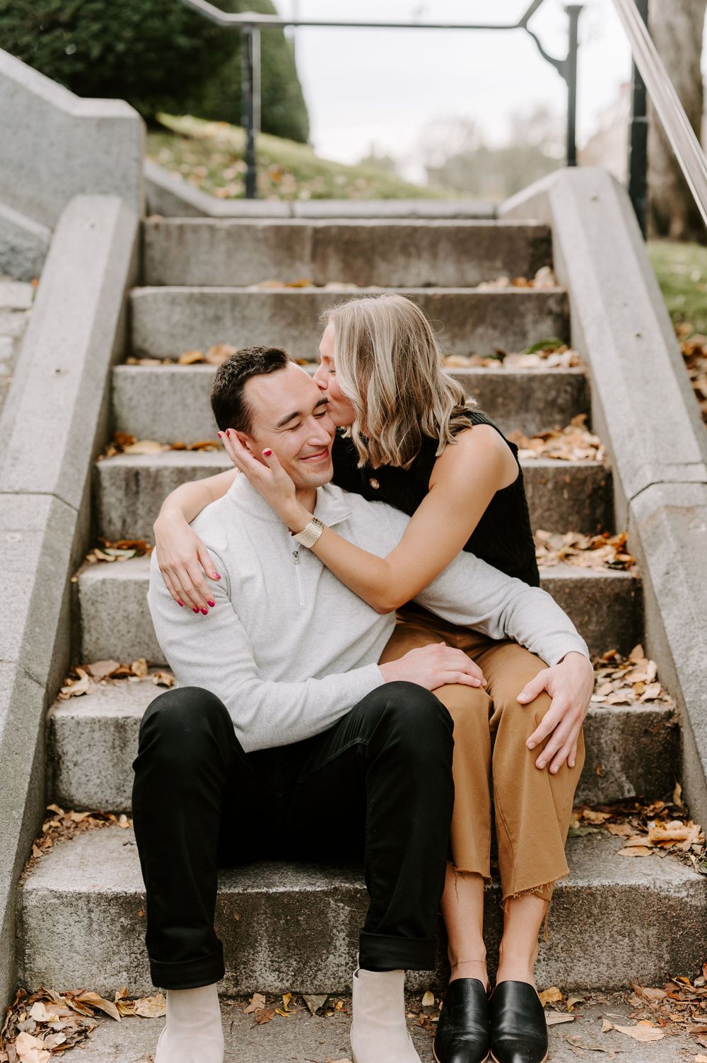 Intimate couple shares tender moment on stone steps covered with fallen leaves.