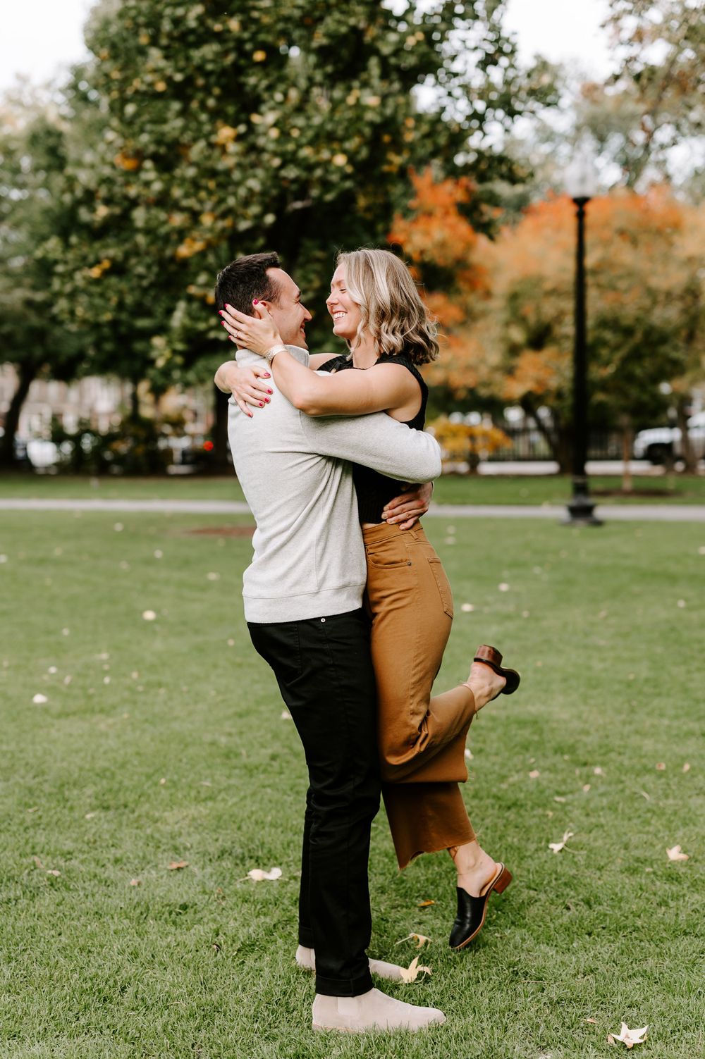 Joyful couple hugging and laughing on green lawn with autumn trees in background.