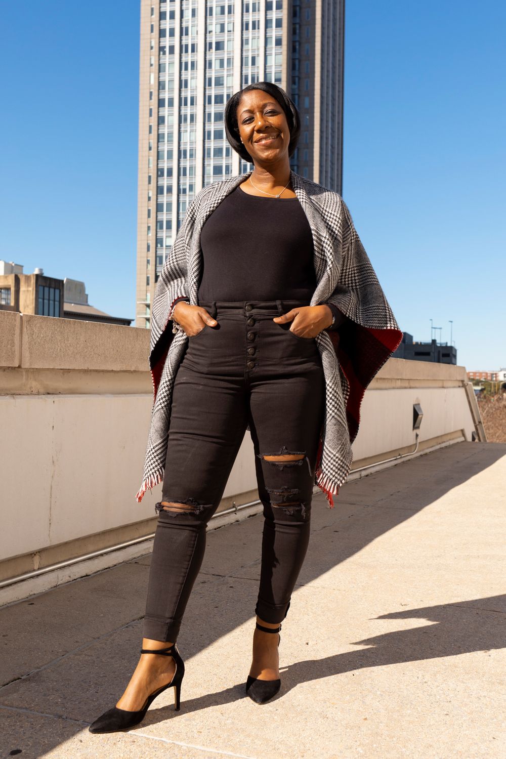A person standing in front of a building with their head titled and hands in their pocket.