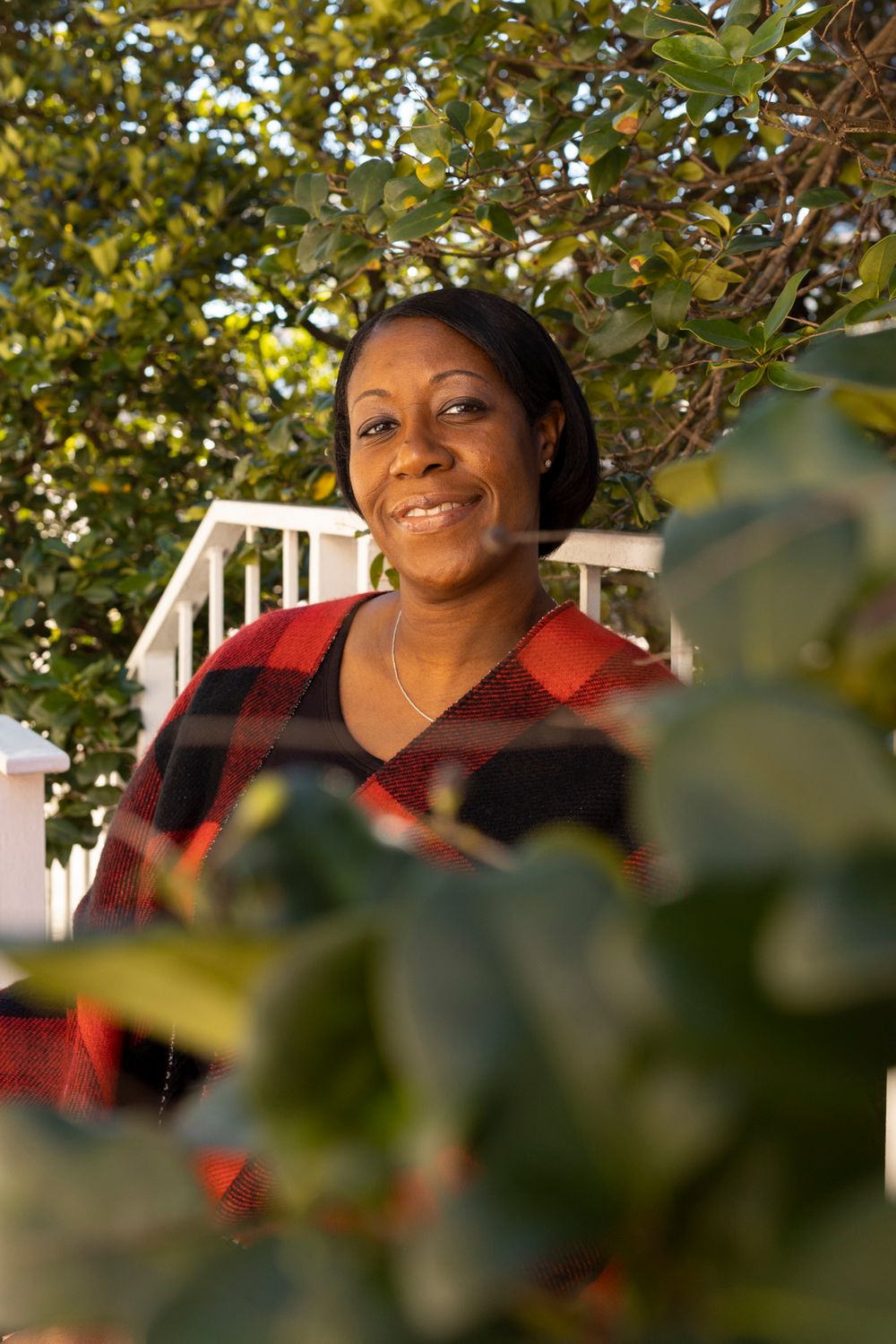 A person wearing a read flannel sitting behind a bush.