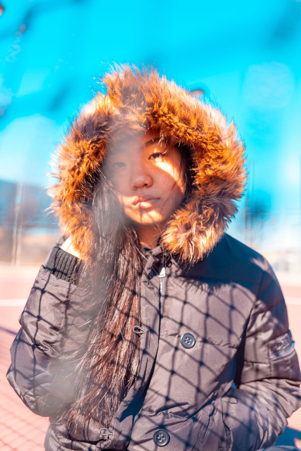 A person wearing a coat posing behind a tennis net.