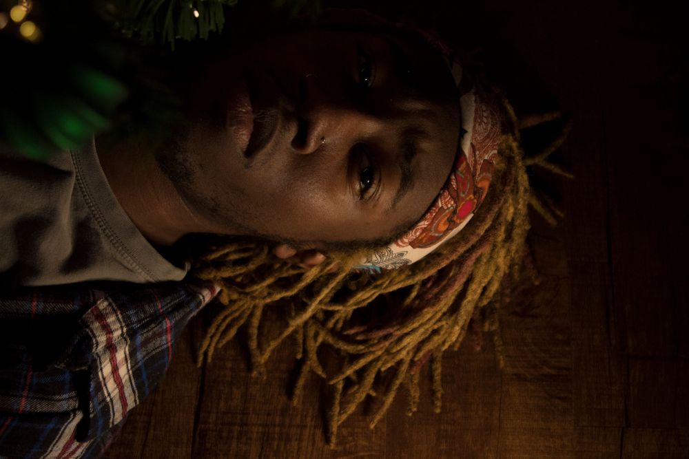 A person wearing a bandana laying on the ground with green branch sticking out.