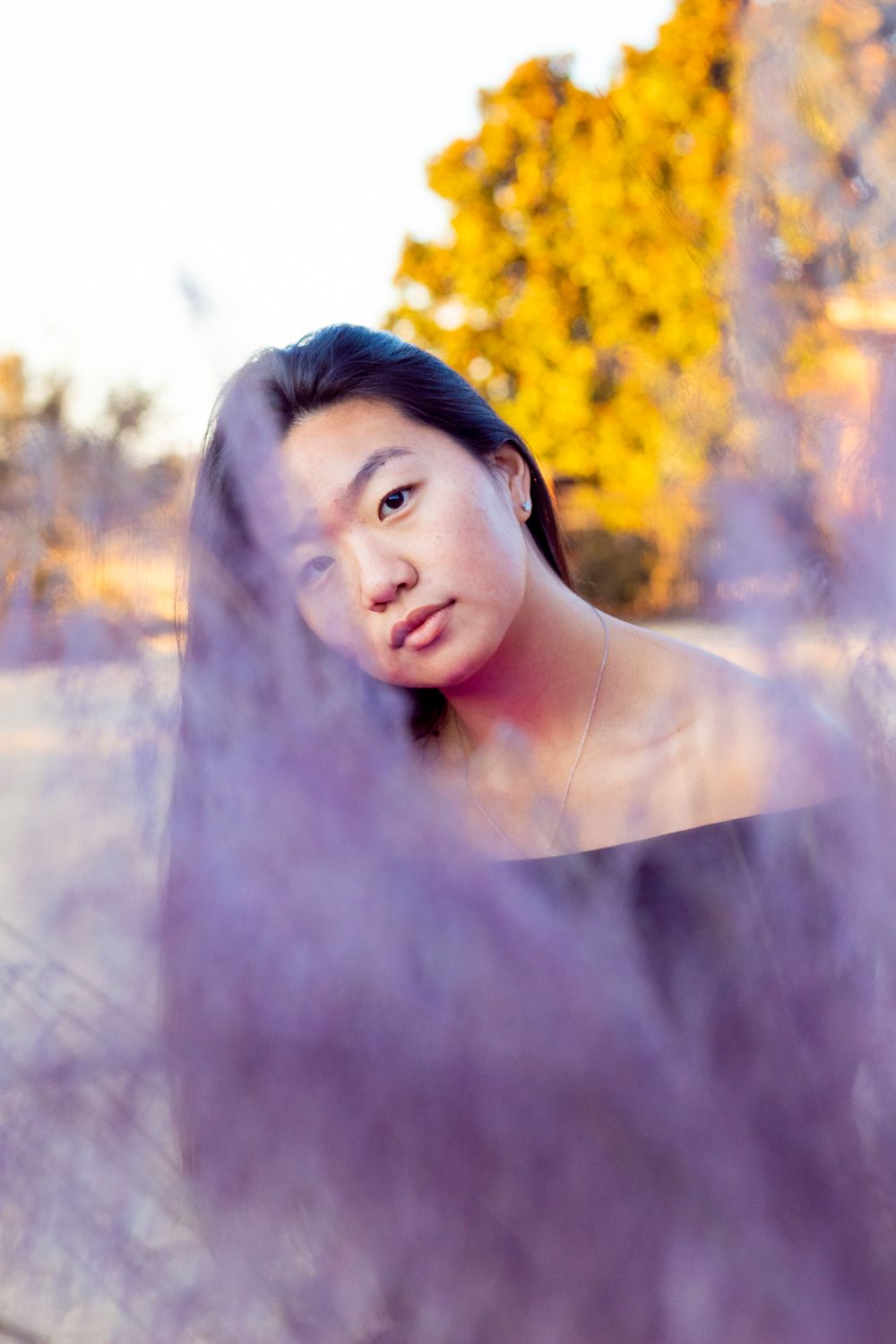 A person with their head titled looking at the camera from behind a lavender bush.