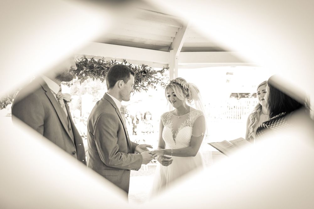 shot through the wooden trellis on the gazebo of the groom putting a ring on the brides finger at west tower