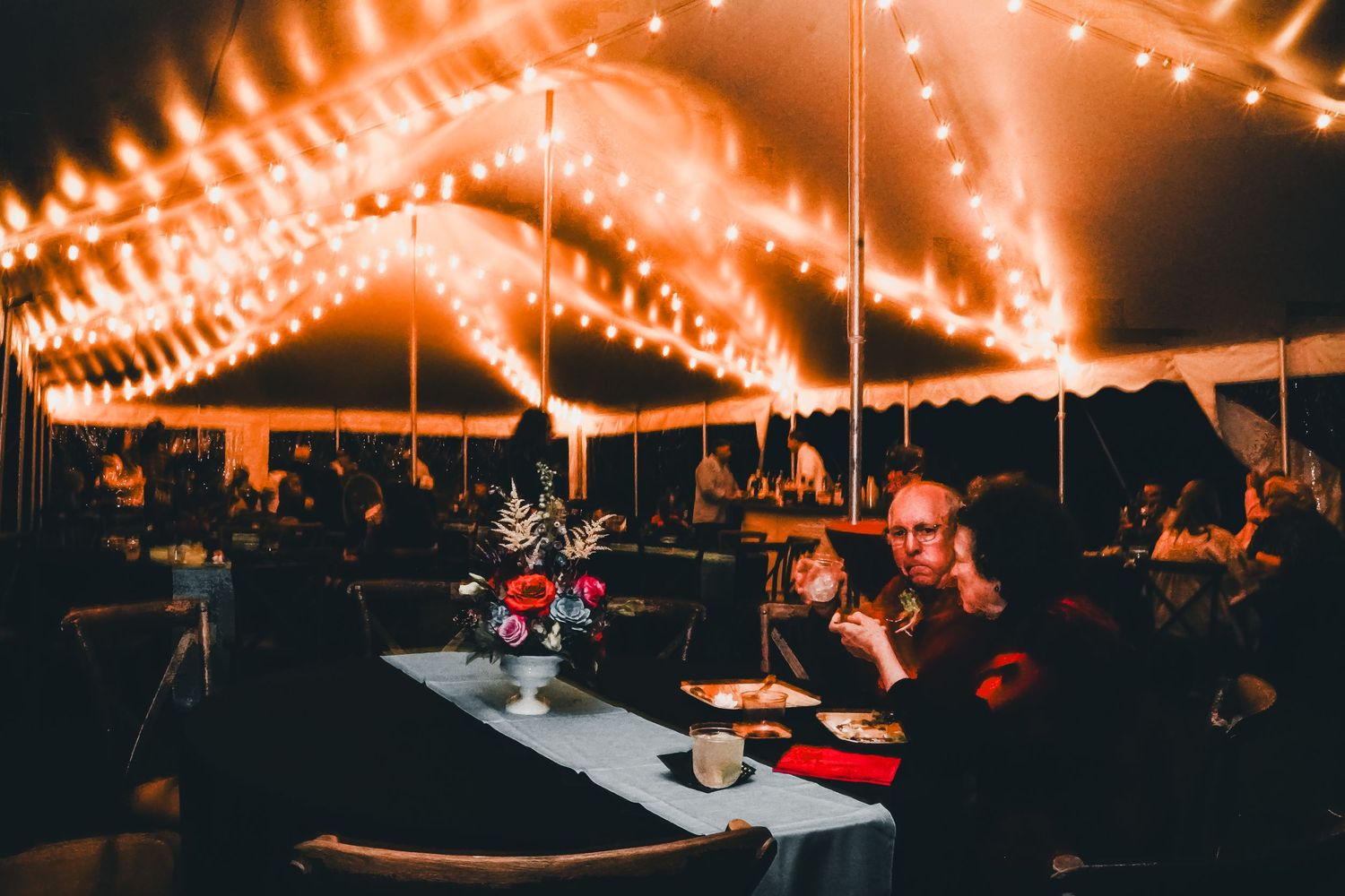 Festive outdoor dining setup with string lights creating warm ambiance at night.