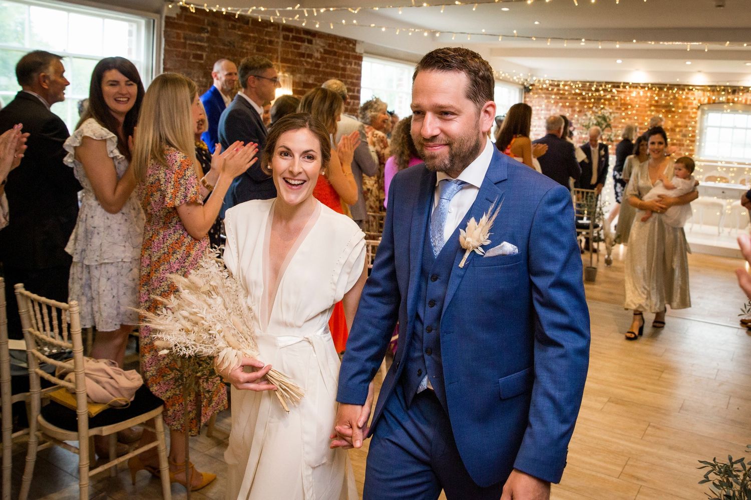 Newlyweds walk down aisle while guests celebrate in reception venue.