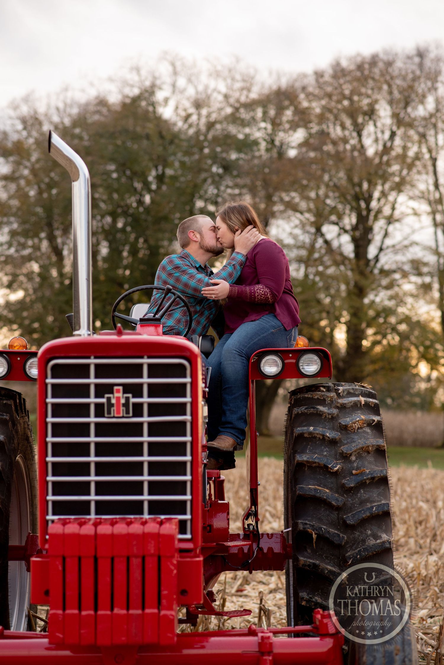 A romantic couple sharing a moment on a bright red vintage tractor at sunset.