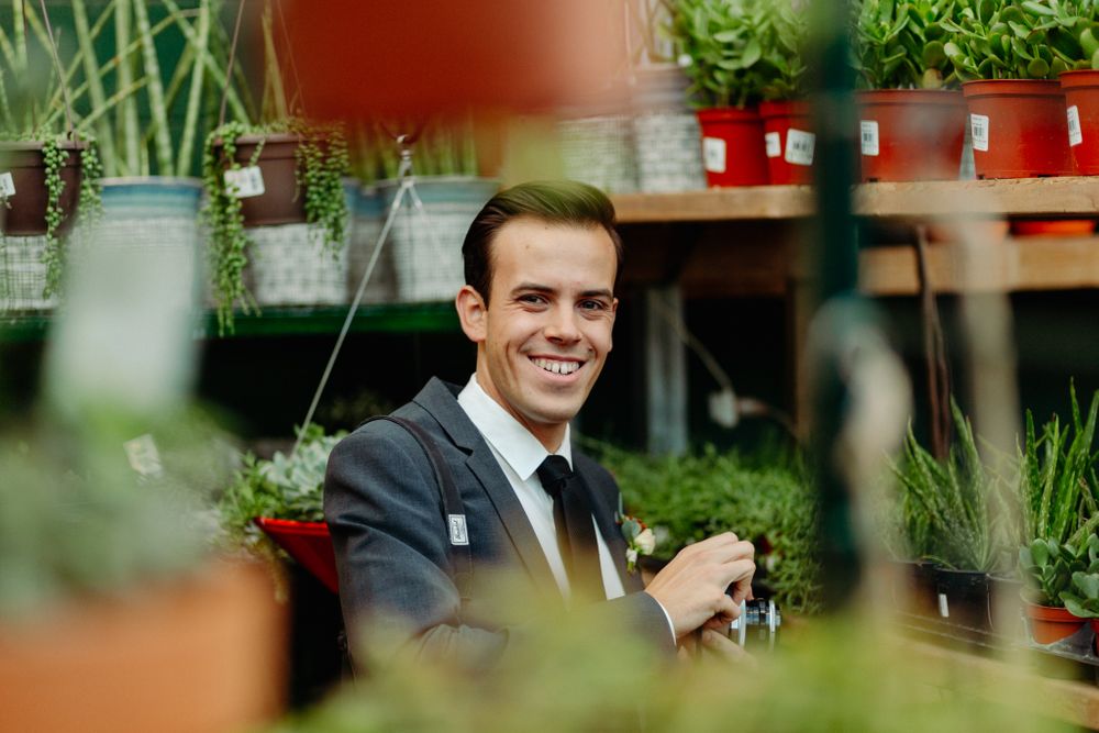 A suited figure among potted plants and greenery in a garden setting.