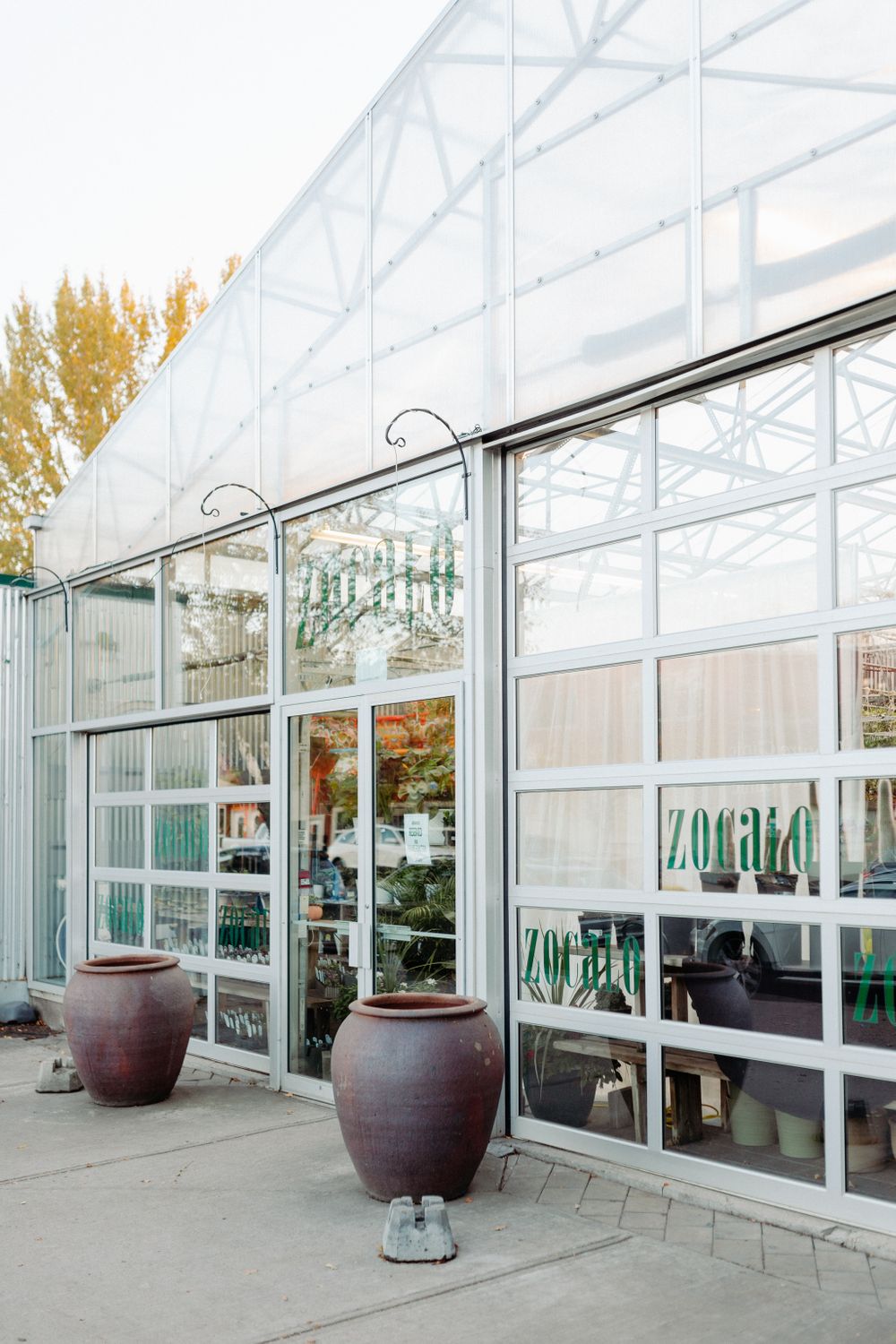 Modern greenhouse exterior with glass panels and large terracotta planters by the entrance.