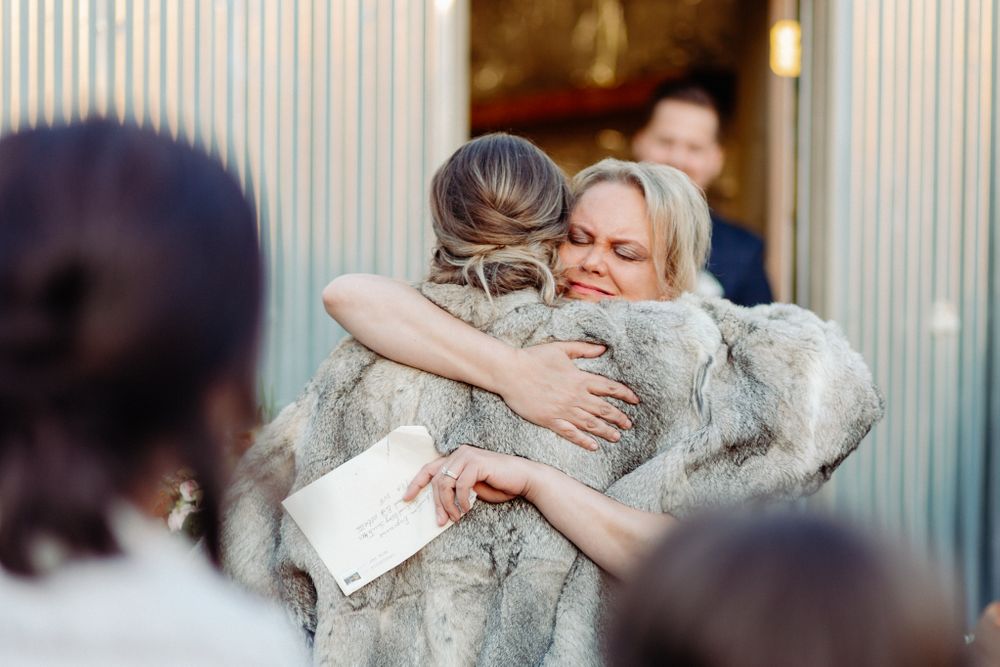 Two people sharing an emotional embrace while holding papers at an event.