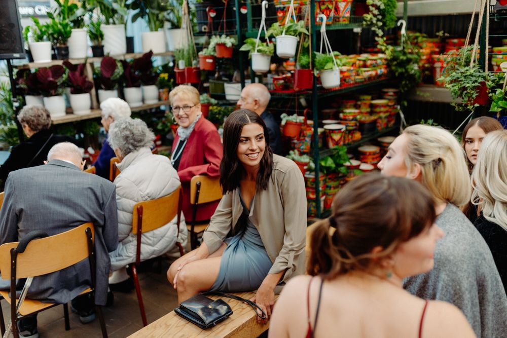 Guests gathered in a restaurant setting with plants and wooden chairs for a celebration.