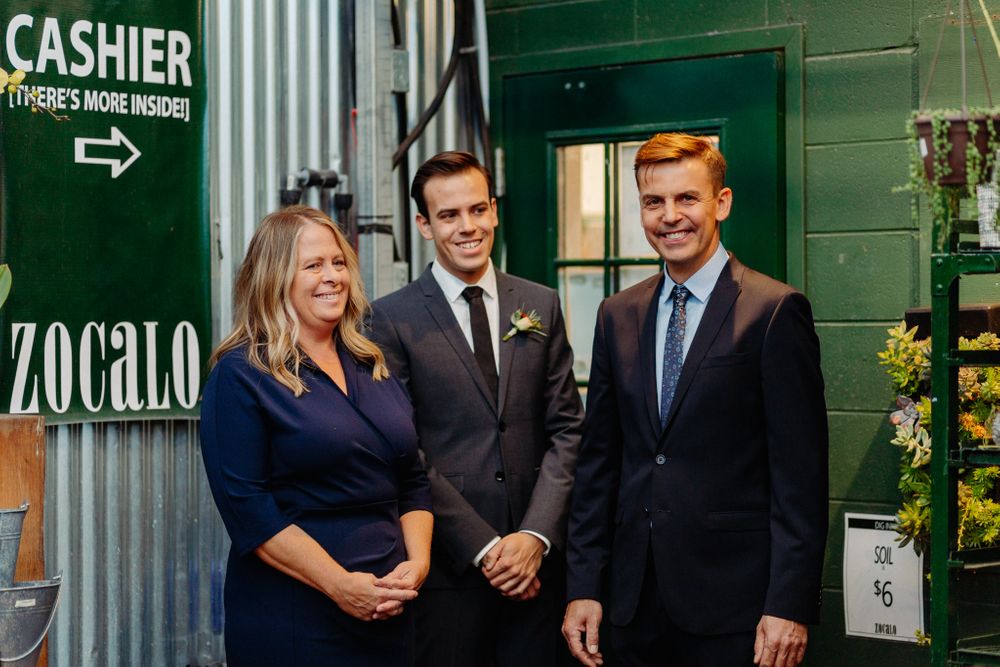 Three professionals in formal attire stand in front of a green storefront with a Zocalo sign.