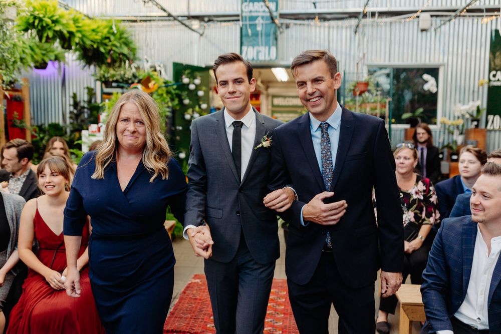 Wedding party members walking down a red carpet aisle during an indoor garden ceremony.