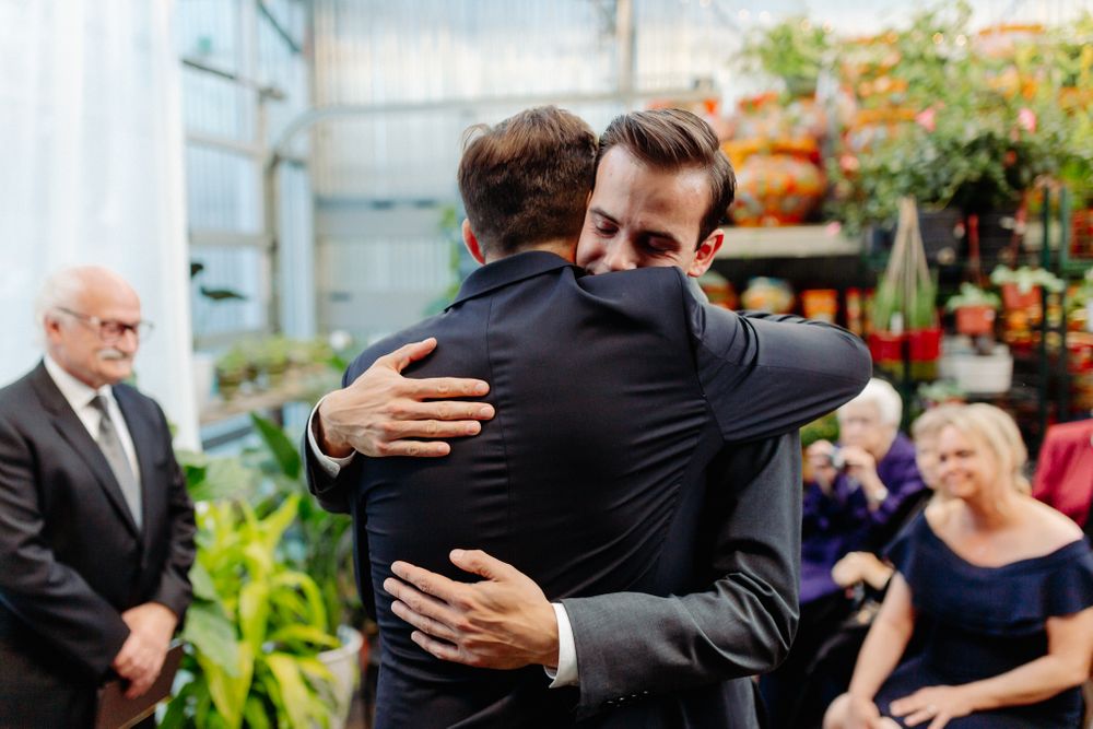 Two people in dark suits share an emotional embrace during a ceremony.