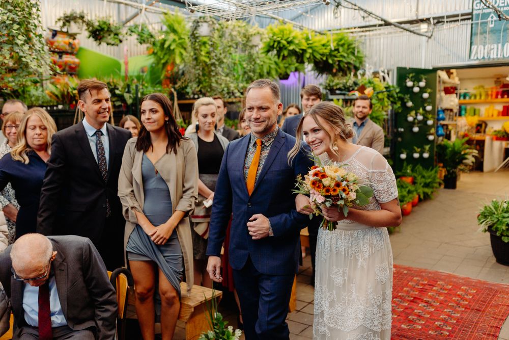 Emotional wedding moment with autumn bouquet in greenhouse surrounded by guests.