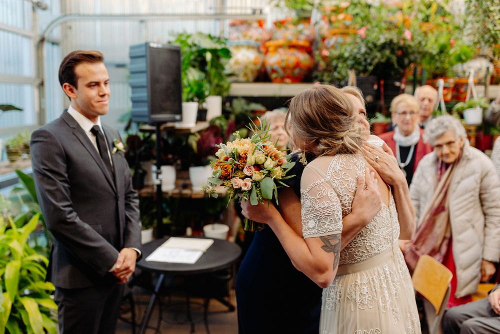 Tender moment during greenhouse wedding ceremony with golden boutonniere detail.