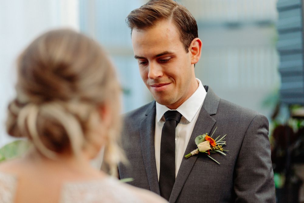 Wedding ceremony with officiant in greenhouse surrounded by white curtains and potted plants.