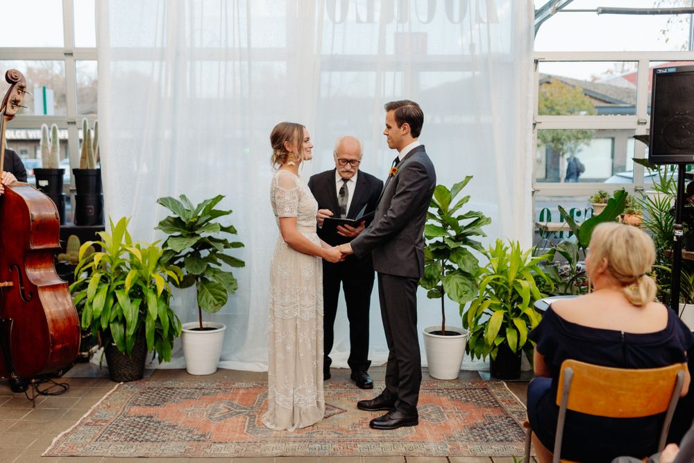 Wide view of greenhouse wedding ceremony with guests seated on both sides of botanical aisle.