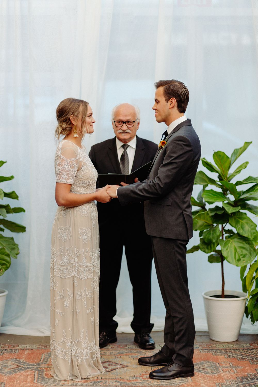 A wedding ceremony in a greenhouse with lush plants and brick flooring.