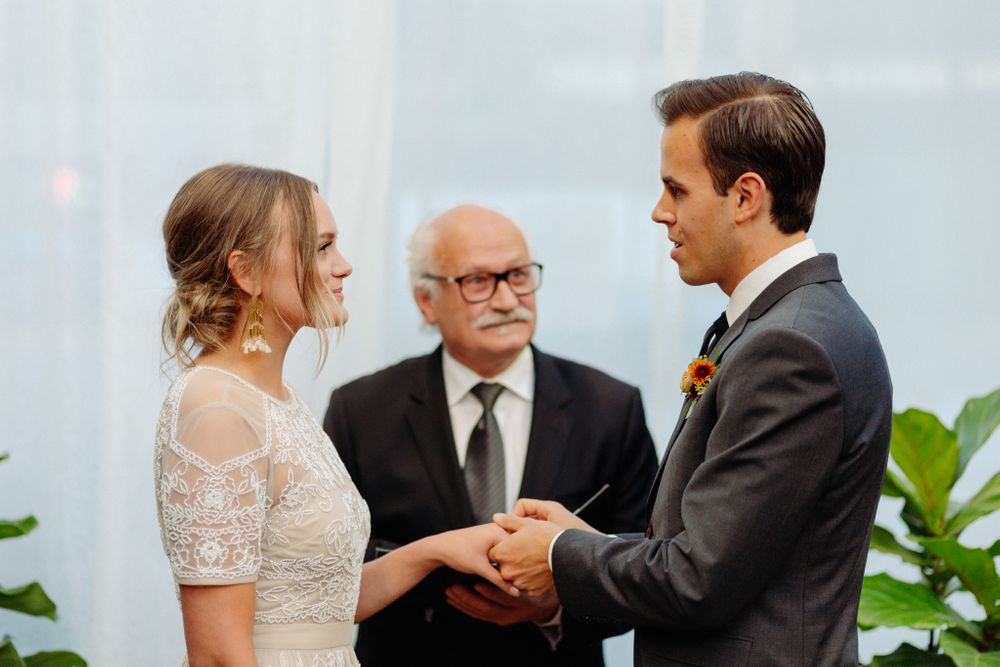 Wedding vows being exchanged in front of white curtains and potted greenery.