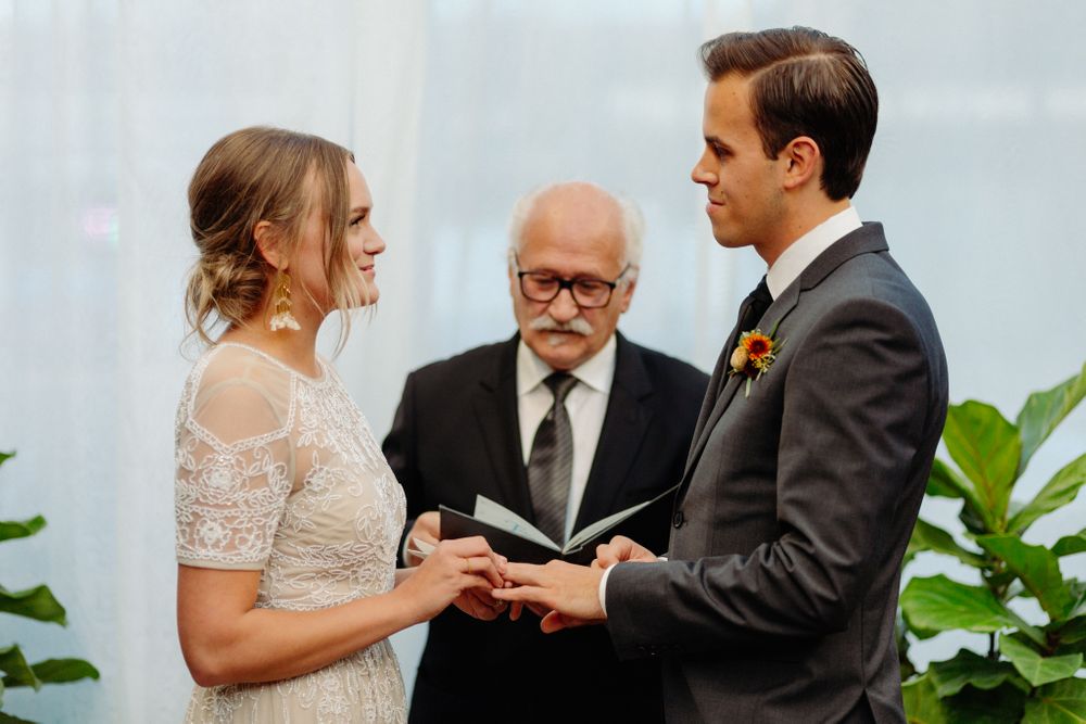 A wedding ceremony taking place in a light-filled greenhouse with tropical plants.