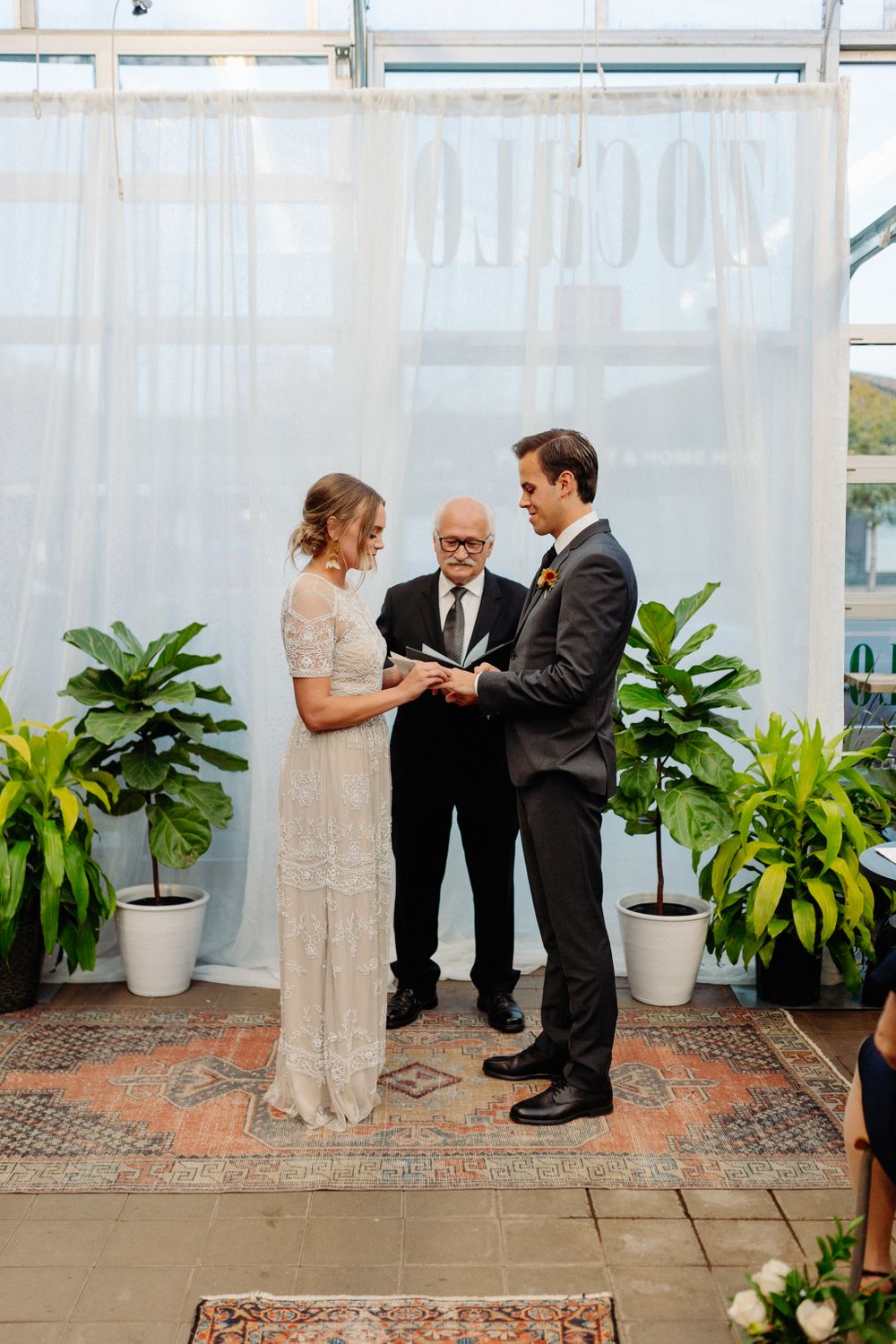 An intimate greenhouse wedding ceremony with white curtains and tropical plants decorating the space.